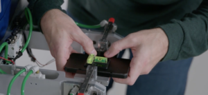 Corning worker holding a demonstration phone with Gorilla Glass on a testing rig, with spirit levels resting on top.